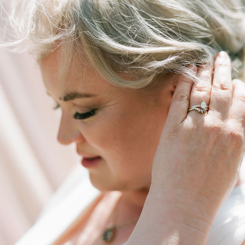 A bride fixes her hair - she wears an engagement ring with a matching wedding band