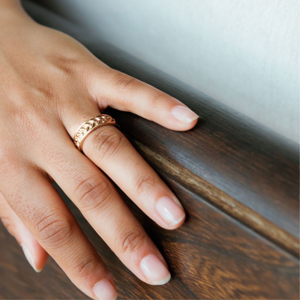 a woman wears a leaf textured gold wedding band, her hand rests on a wooden pew