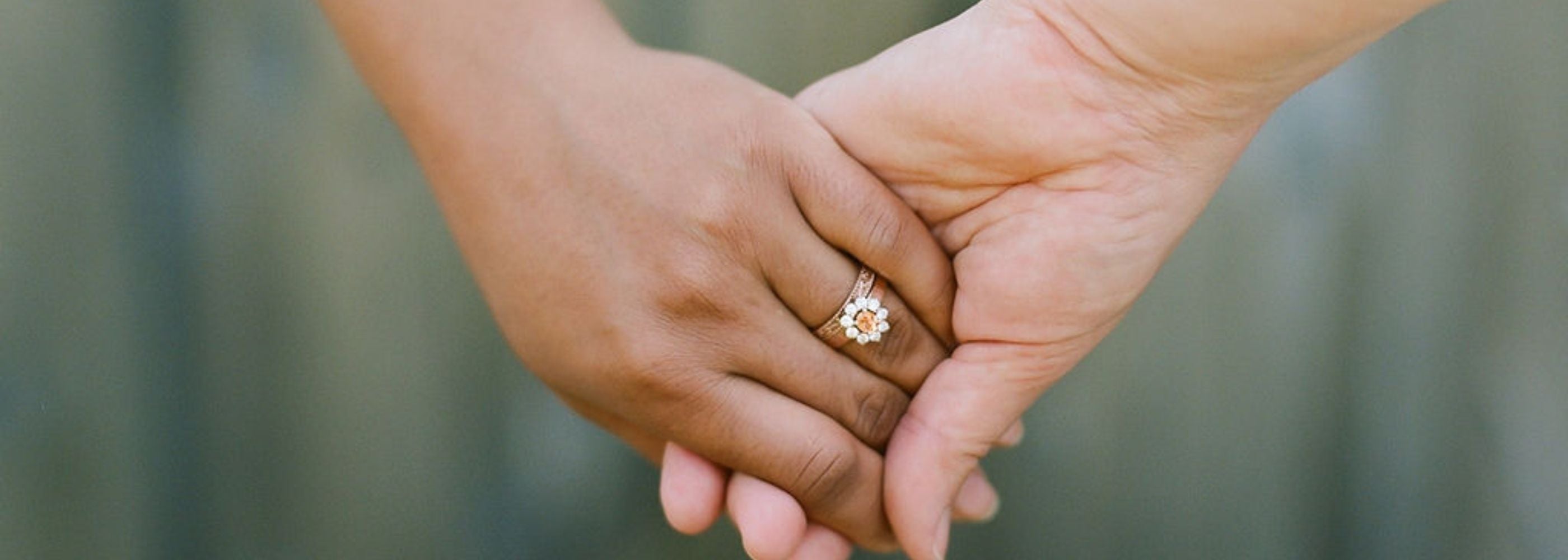 two women hold hands, a colourful pink engagement ring with halo is worn