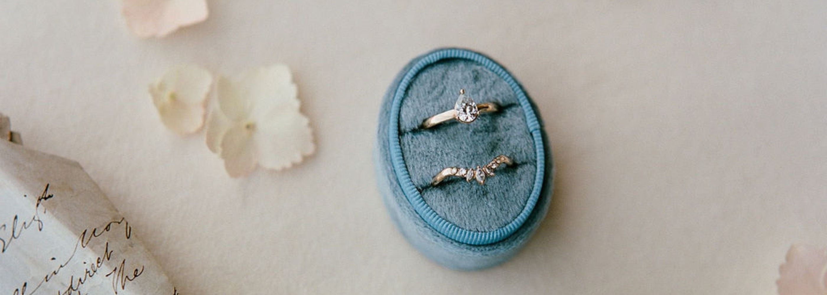 a moissanite pear engagement ring and matching curved wedding band with marquise moissanites are displayed in a blue velvet box