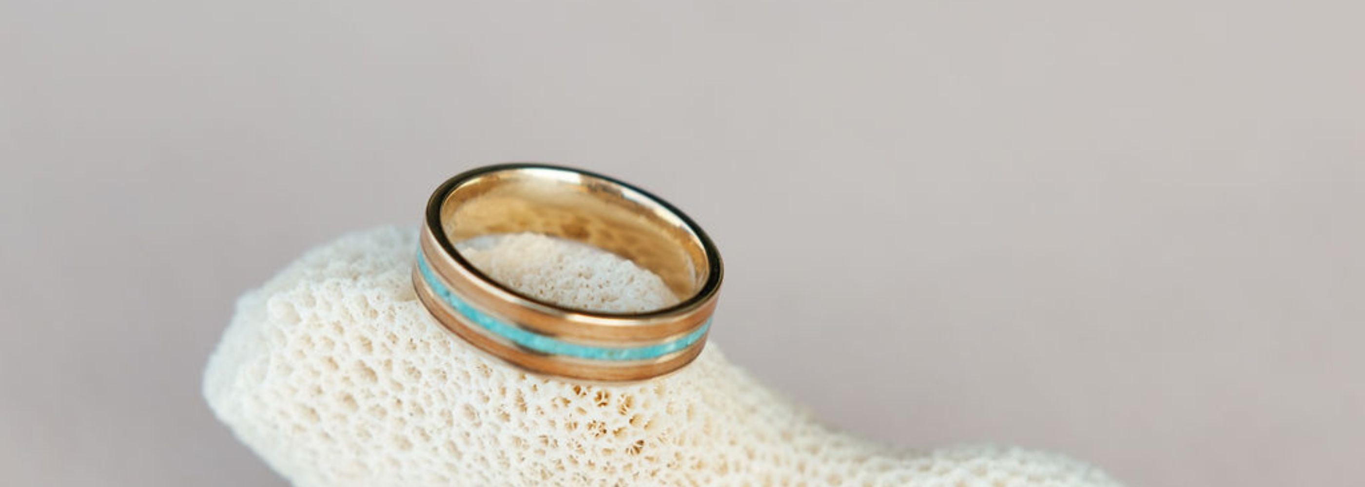 a wood inlay ring featuring red alder and turquoise sits atop dried white coral