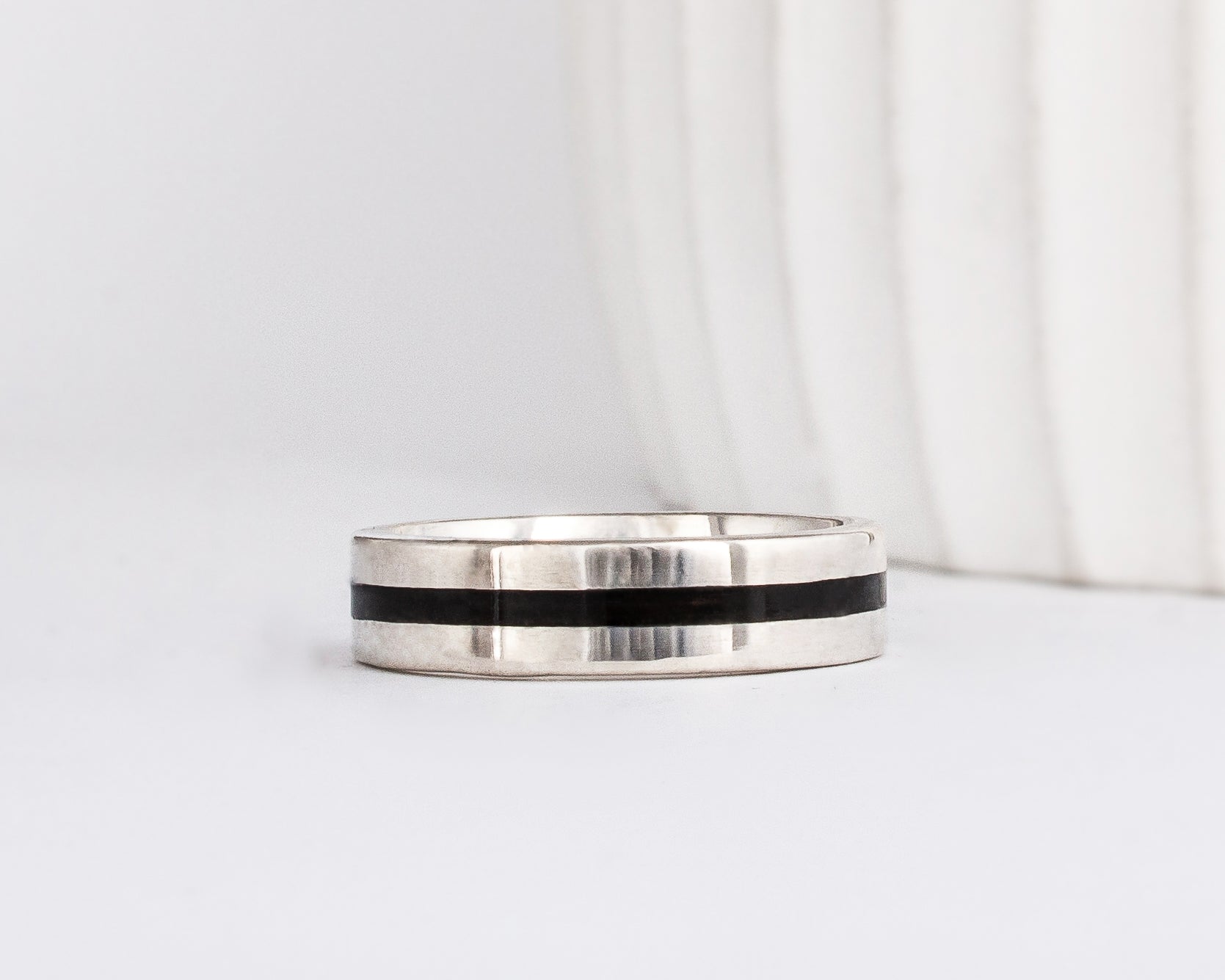 a modern wooden wedding ring for men or women featuring white gold, a flat profile and a central inlay of dark black ebony wood