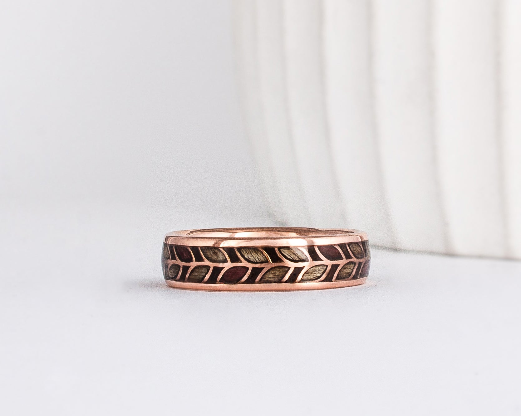 a unique wooden ring, made from rose gold with a delicate laurel leaf floral pattern. Each leaf is filled with wood - alternating between grey maple and purpleheart wood