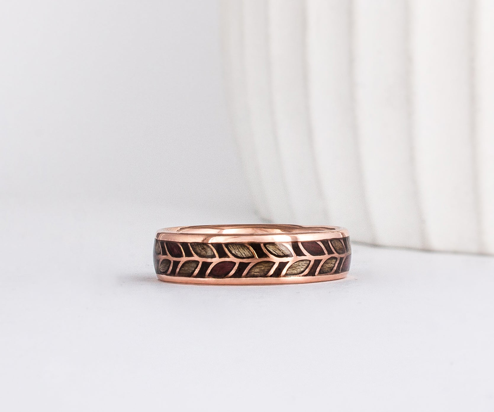 a unique wooden ring, made from rose gold with a delicate laurel leaf floral pattern. Each leaf is filled with wood - alternating between grey maple and purpleheart wood
