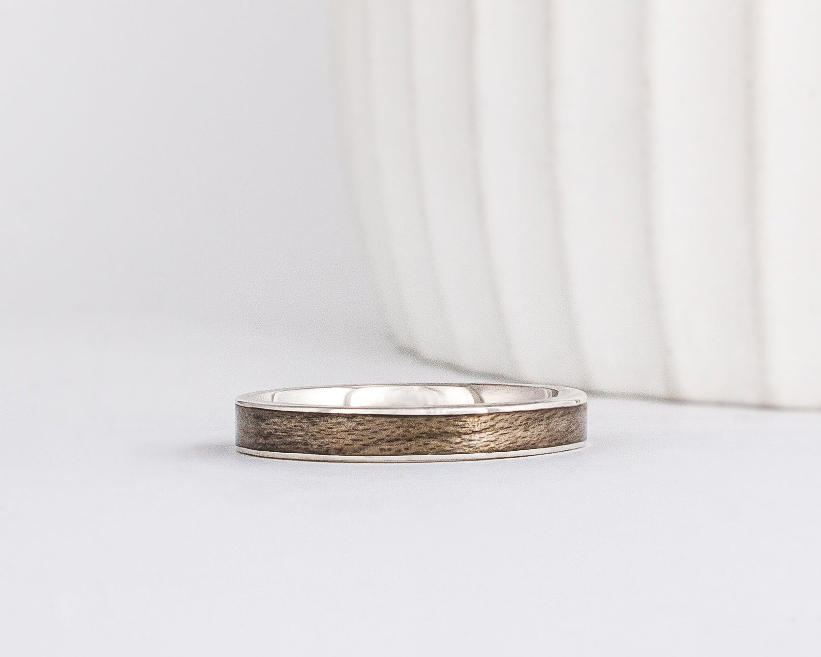 white gold band with a straight edge profile with thin gold borders outlining a neutral gray inlay of maple wood