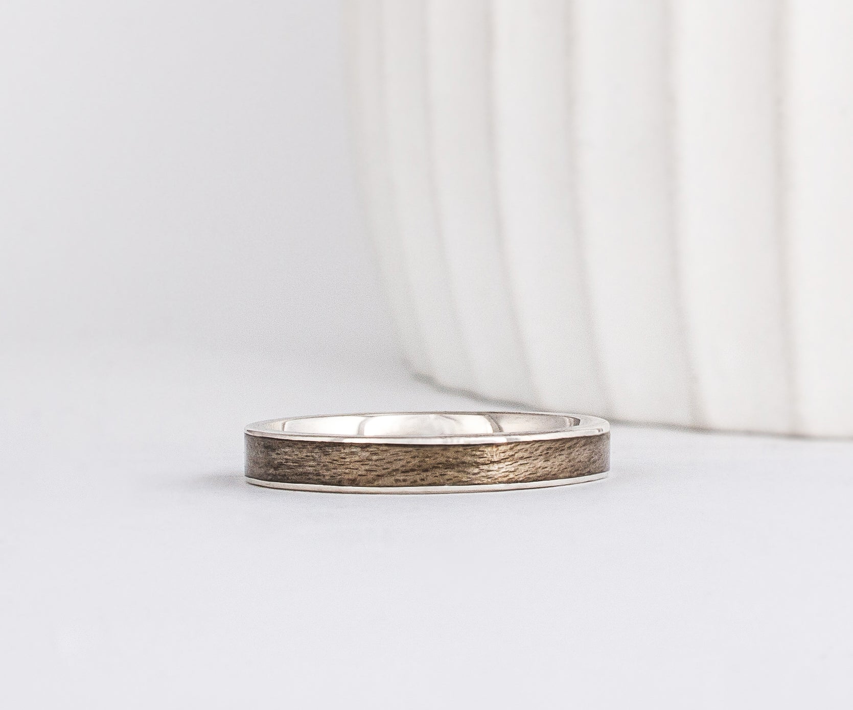 white gold band with a straight edge profile with thin gold borders outlining a neutral gray inlay of maple wood