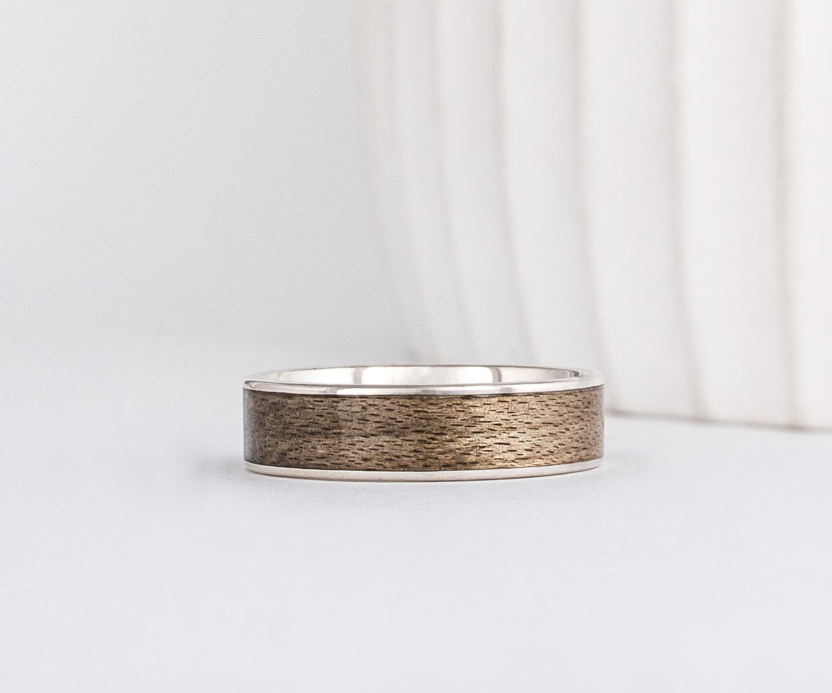 a white gold ring is inlaid with grey maple wood that has a distinct grainy appearance