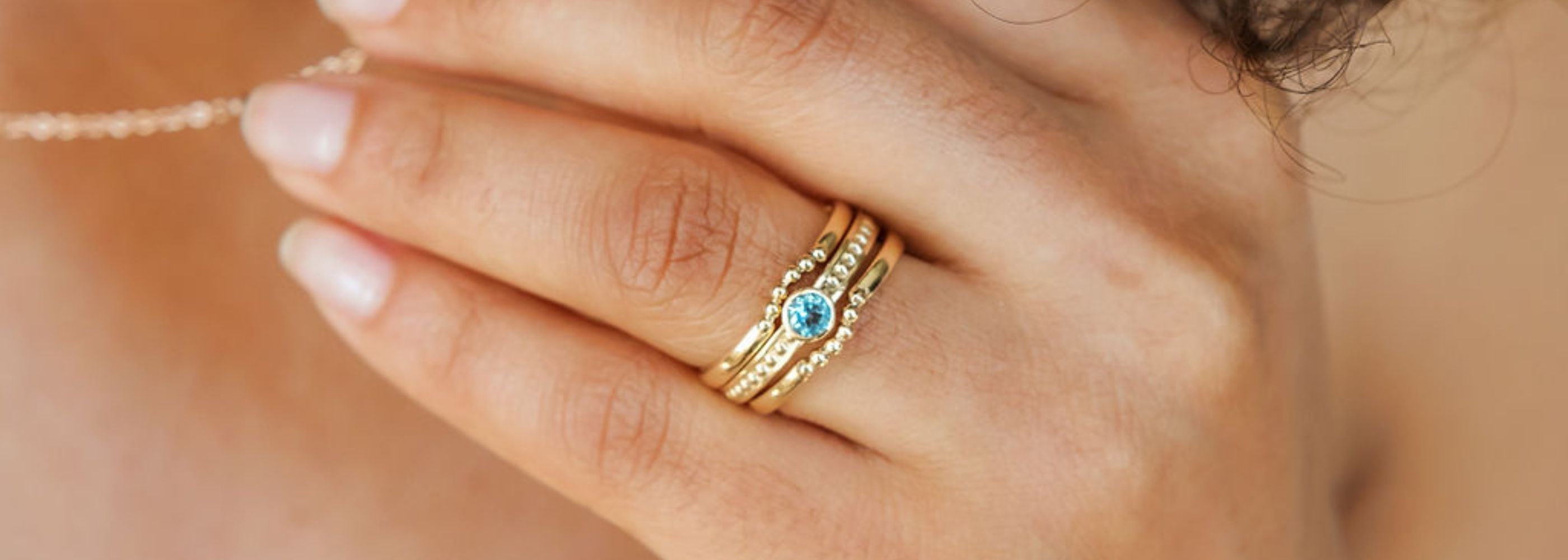 a woman wears a set of rings with a blue aquamarine bezel set in the center of a stack