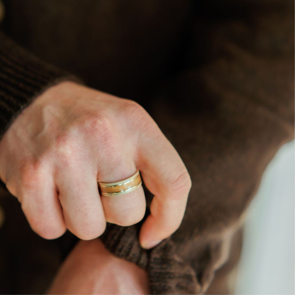 a man wears a gold milgrain detail ring with a wood inlay in the middle. he fixes his sleeve.