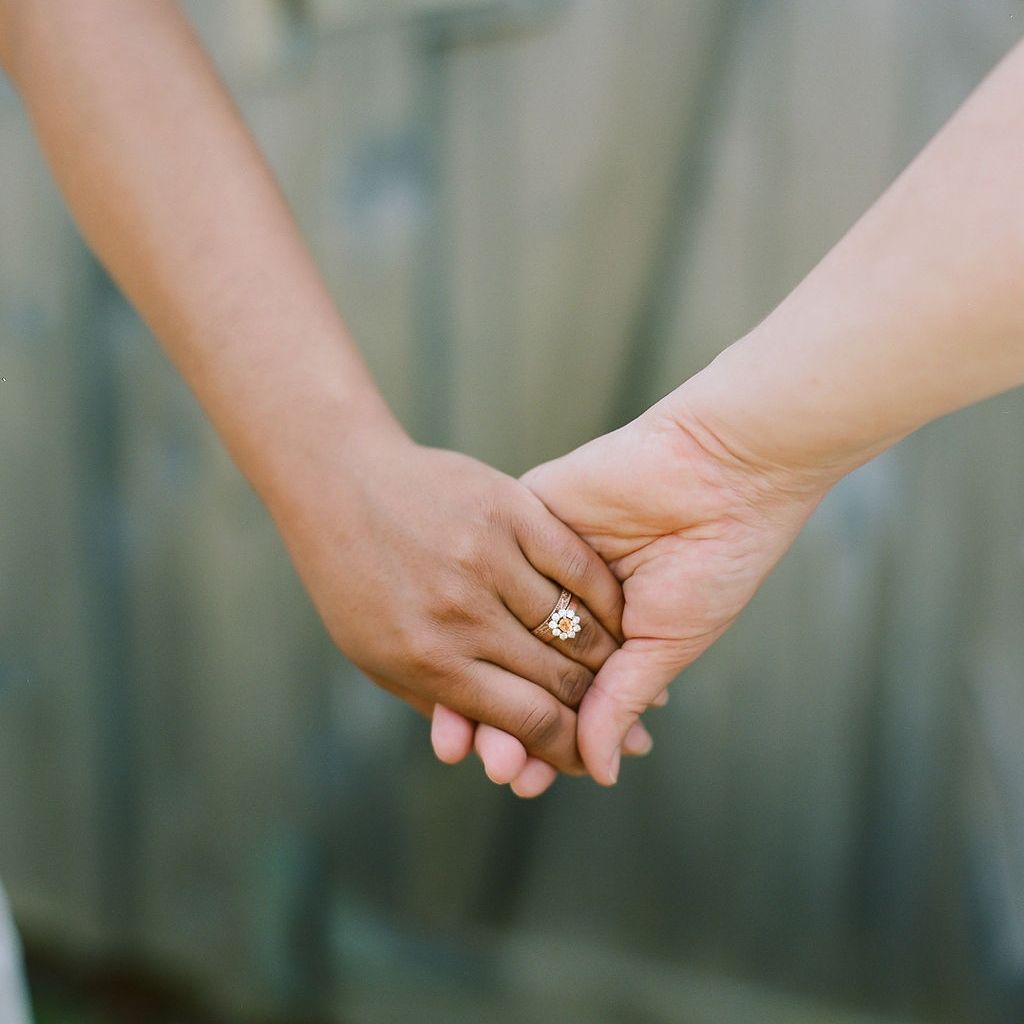 two women hold hands, you can see one wears a halo engagement ring