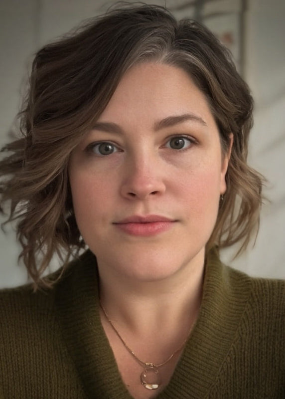Woman with short brown hair wearing a green sweater and gold necklace against a neutral background