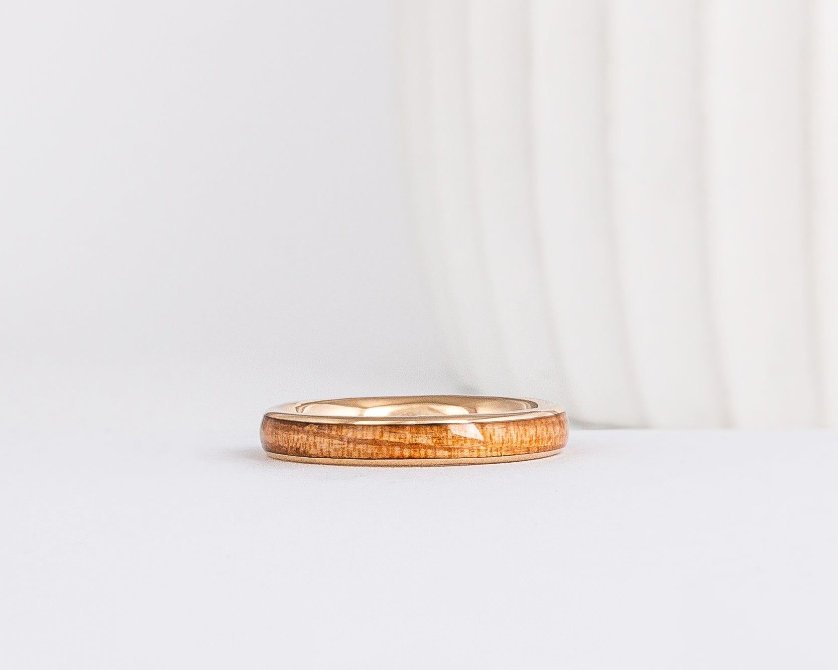 a slim, rounded yellow gold wedding band with a center inlay of american elm wood, giving it a tone on tone look