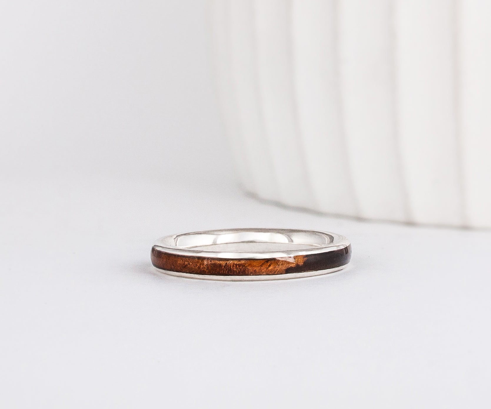 a slim, rounded white gold wedding band with a center inlay of walnut burl wood, giving it a tone on tone look