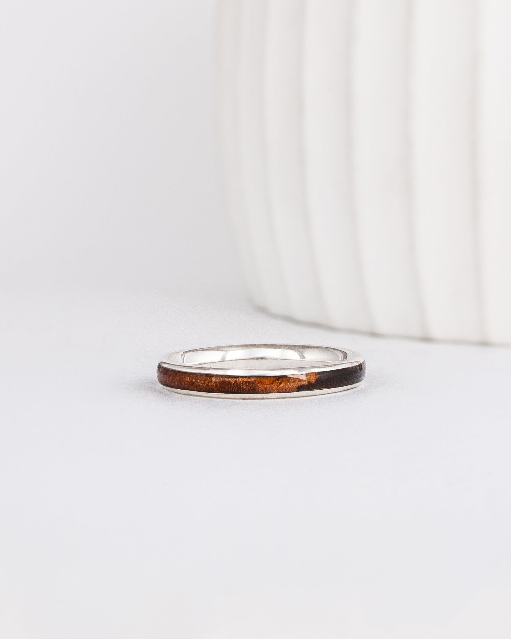 a slim, rounded white gold wedding band with a center inlay of walnut burl wood, giving it a tone on tone look