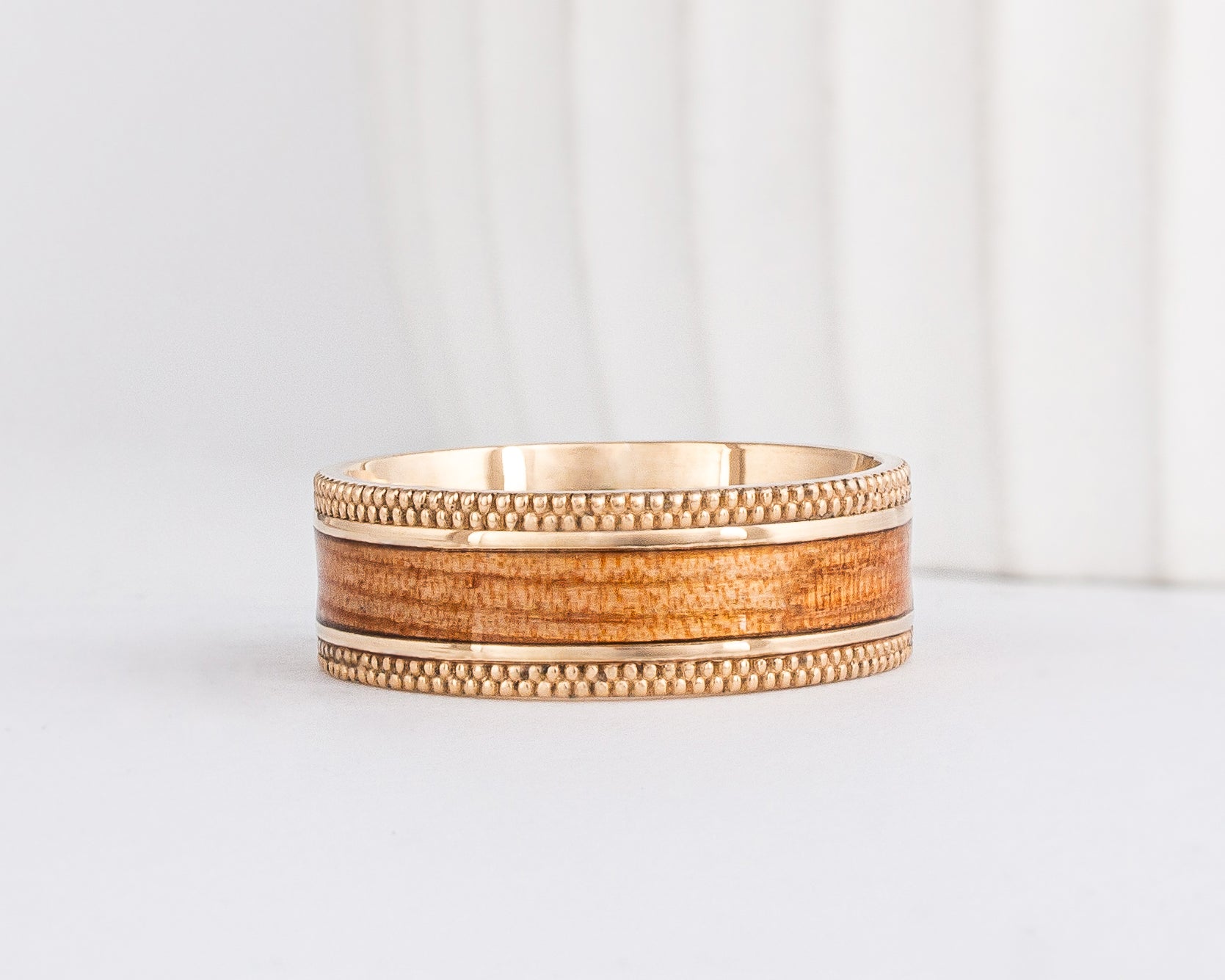 a wide mens wood wedding ring is made from yellow gold and has edges with a double milgrain pattern. The center of the ring is two thin borders of gold on either side of an american elm wood inlay
