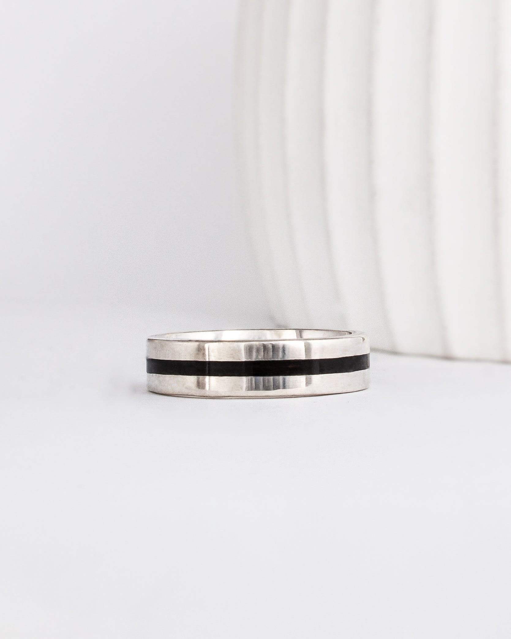 a modern wooden wedding ring for men or women featuring white gold, a flat profile and a central inlay of dark black ebony wood