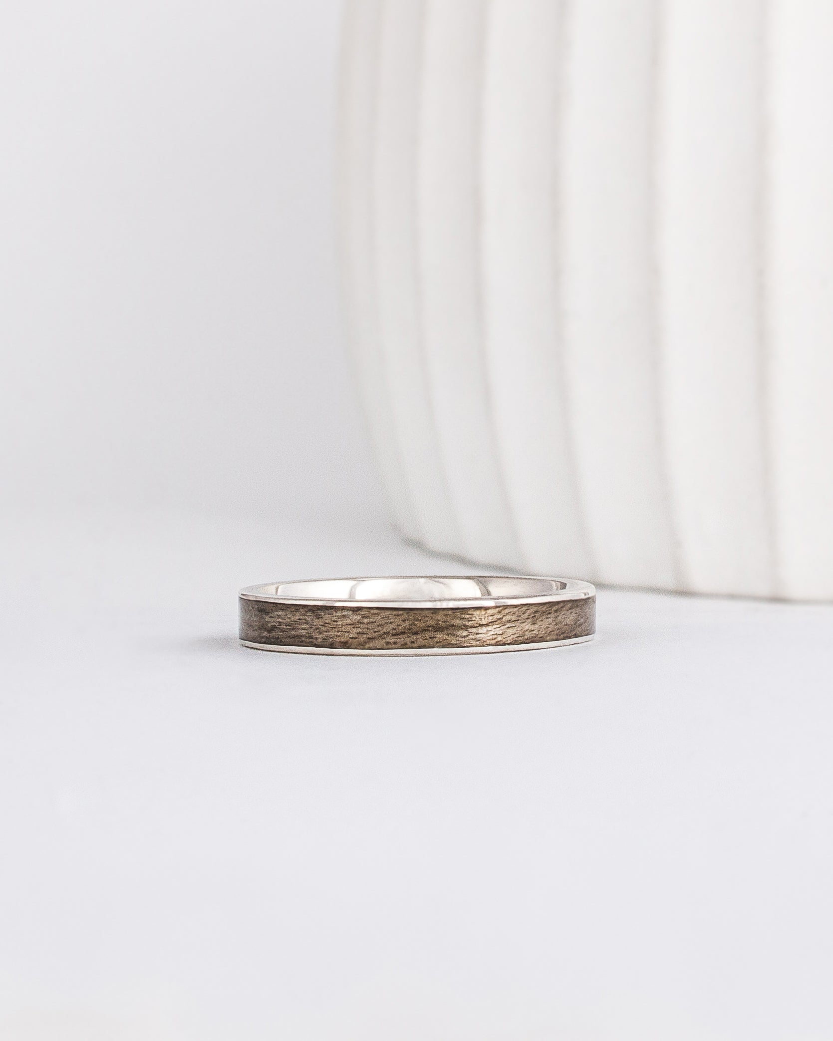 white gold band with a straight edge profile with thin gold borders outlining a neutral gray inlay of maple wood