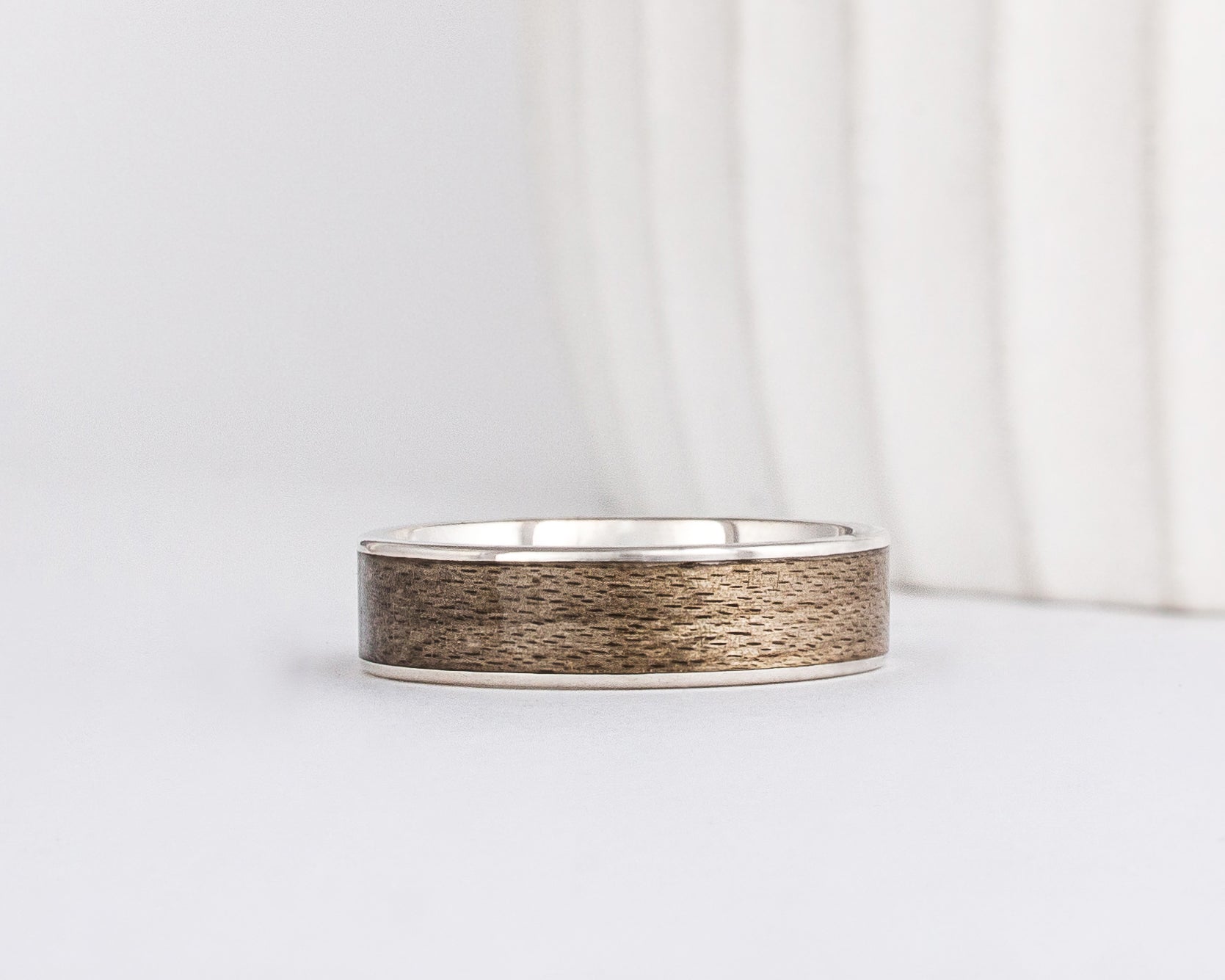a white gold ring is inlaid with grey maple wood that has a distinct grainy appearance