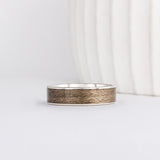 a white gold ring is inlaid with grey maple wood that has a distinct grainy appearance