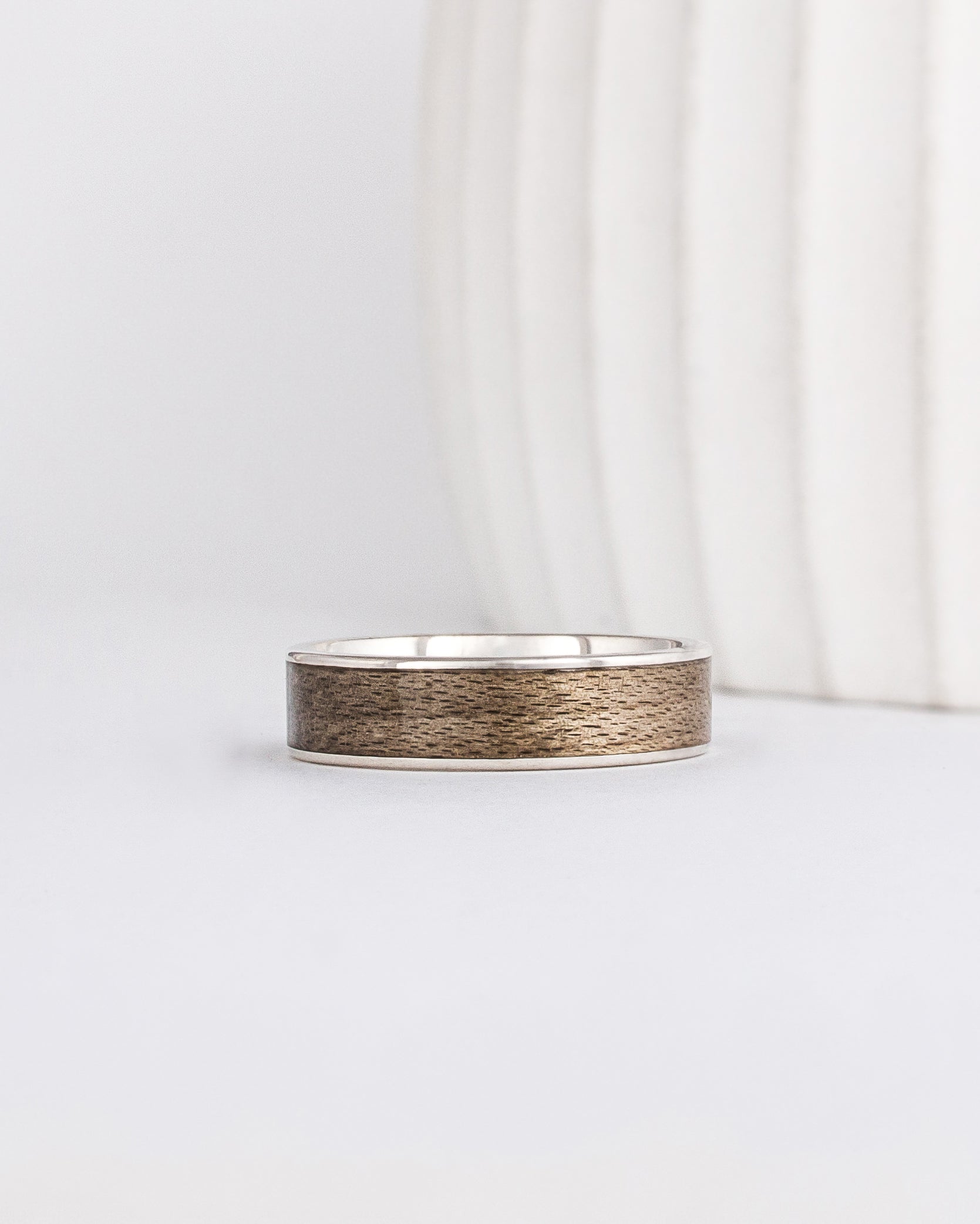 a white gold ring is inlaid with grey maple wood that has a distinct grainy appearance