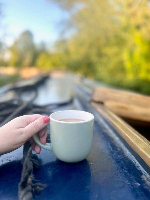 Hand holding a mug of tea on a boat with a scenic background