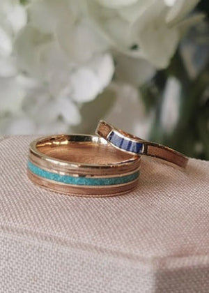 Two gold rings with turquoise inlay on a light fabric surface with a blurred floral background.