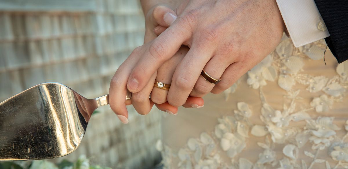 Close-up of hands wearing wood rings, holding a wedding cake knife with a blurred background
