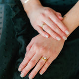 a woman's hand rests on a green dress, she is wearing a wedding ring set featuring a moissanite engagement ring and wood rings with american elm inlays