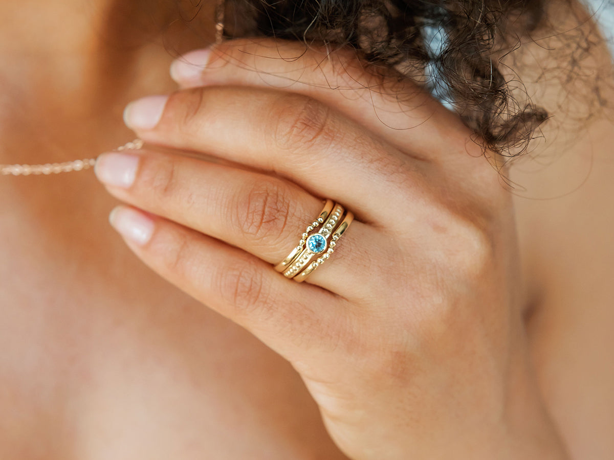 A woman's hand shown wearing the aquamarine bezel set engagement ring along with two delicate ring enhancers to match