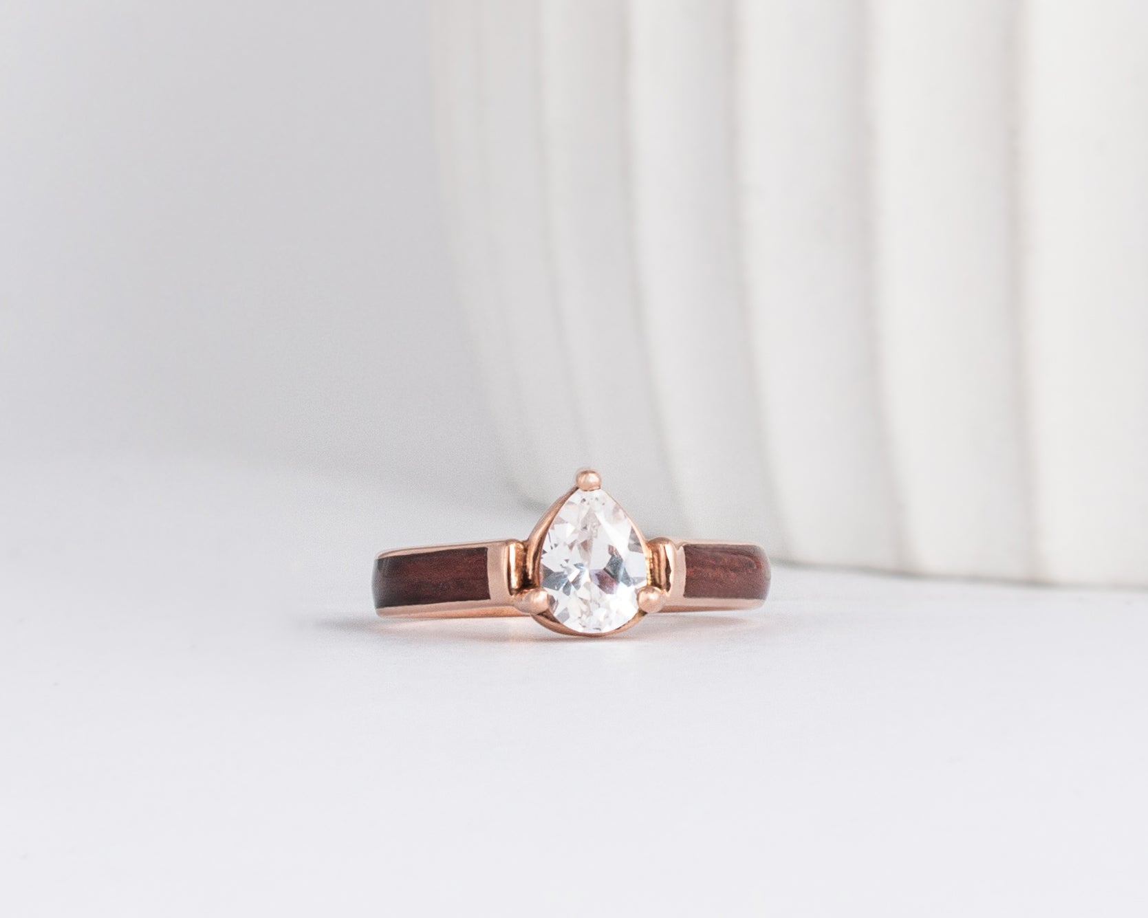 rose gold and purpleheart wood inlay engagement ring featuring a pear shaped moissanite solitaire stone