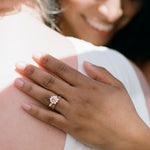 a woman hugs another, her hand shows a filigree wedding band beside a sapphire halo engagement ring
