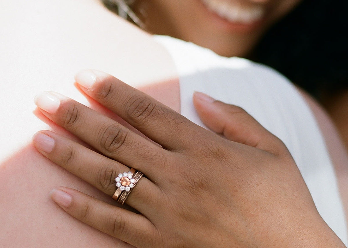 a woman hugs another, her hand shows a filigree wedding band beside a sapphire halo engagement ring