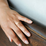 a woman's hand rests on a wooden pew, showing off a wide nature inspired laurel leaf ring